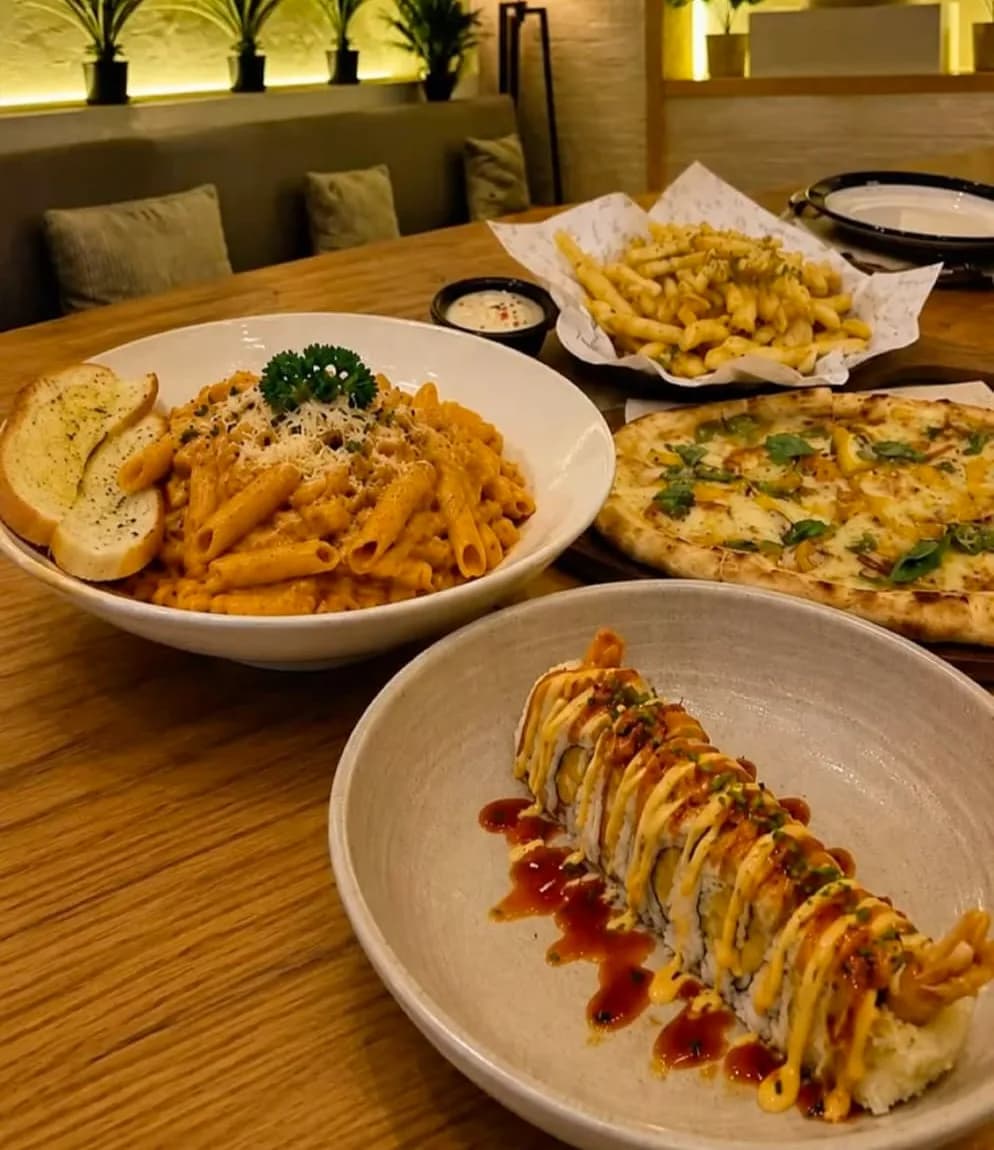 Pink sauce penne with garlic bread, truffle fries, a burrata pizza and a sushi roll on a walnut table, lit by warm niche lights